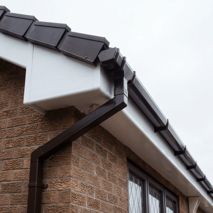Close-up of dark guttering and white soffit along a brick house wall beneath a grey tiled roof.